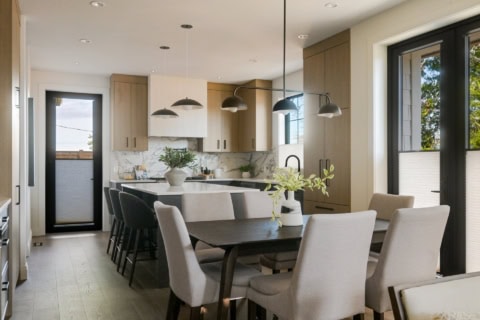 Modern kitchen with island, pendant lights, and dining area in Cedar & Stone project by White Wolf Homes.