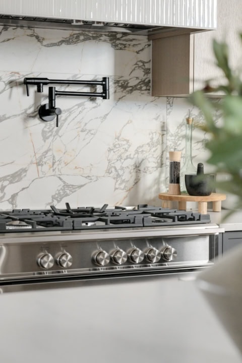 Modern kitchen stove with marble backsplash and black faucet in Cedar & Stone home by White Wolf Homes.