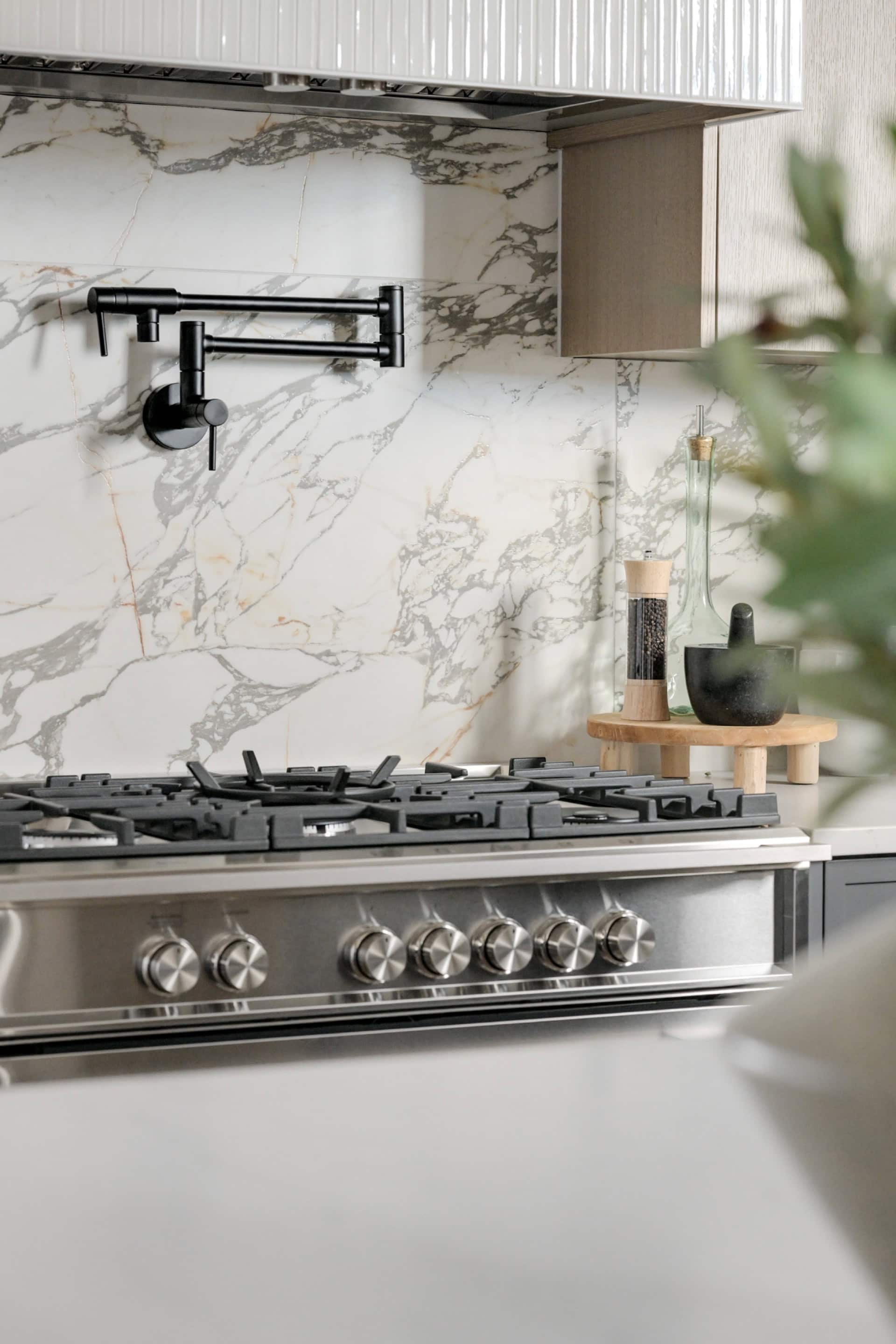 Modern kitchen stove with marble backsplash and black faucet in Cedar & Stone home by White Wolf Homes.