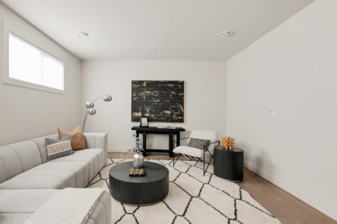 Modern living room with light gray sectional, geometric rug, and contemporary furniture in a clean white space.