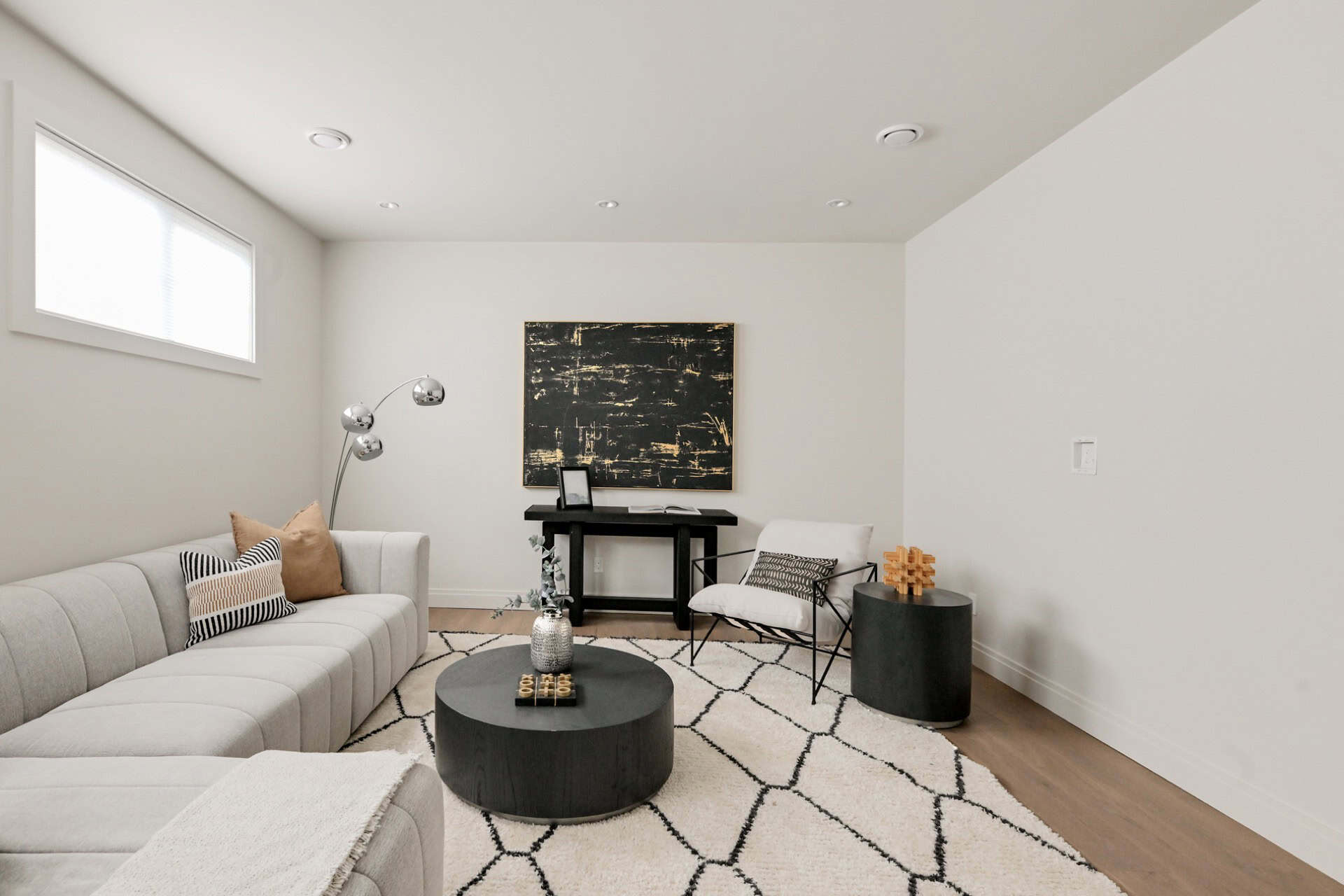 Modern living room with light gray sectional, geometric rug, and contemporary furniture in a clean white space.