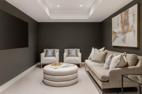 Cozy basement living room with neutral sofa, lounge chairs, modern ottoman and dark accent wall.