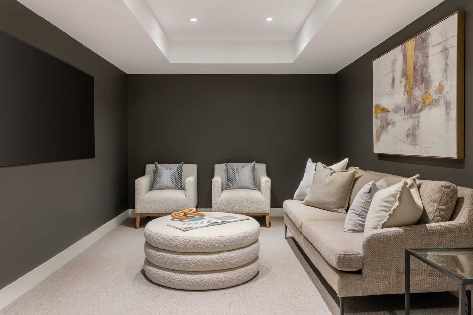 Cozy basement living room with neutral sofa, lounge chairs, modern ottoman and dark accent wall.
