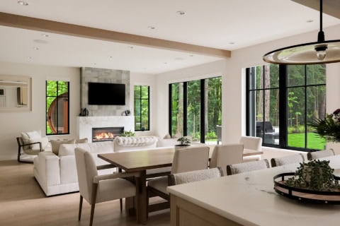 Bright open-plan living and dining area with large windows, fireplace, and neutral furnishings.
