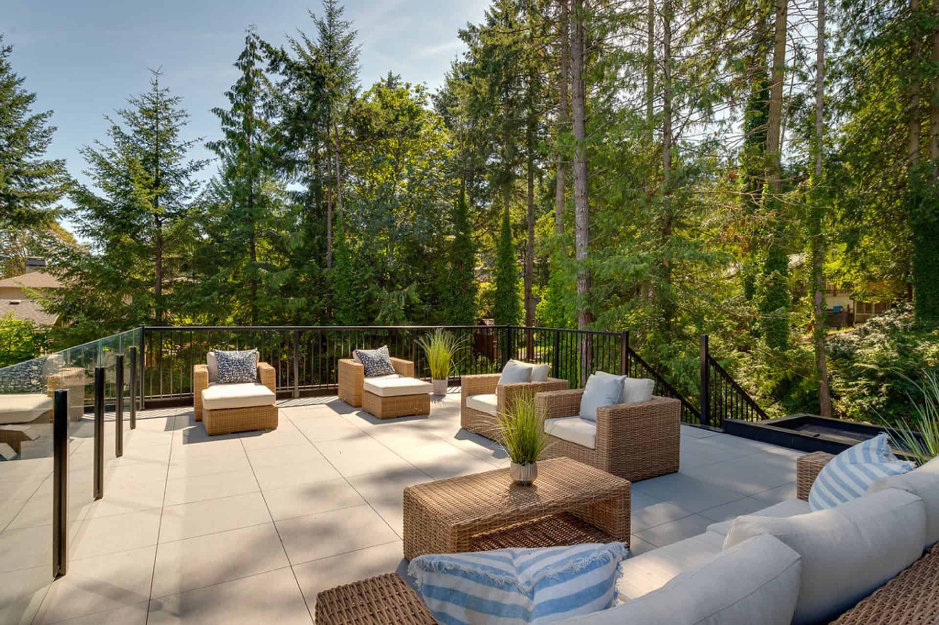 Outdoor living area with wicker seating on a terrace surrounded by tall evergreen trees.