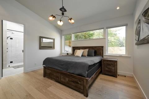 Bright bedroom with wooden bed frame and large windows in a modern home.