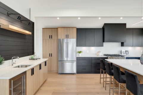 Modern kitchen with light wood and dark gray cabinetry, stainless fridge, island seating.