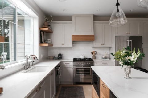 Modern white kitchen with island, stainless steel appliances, and large window.