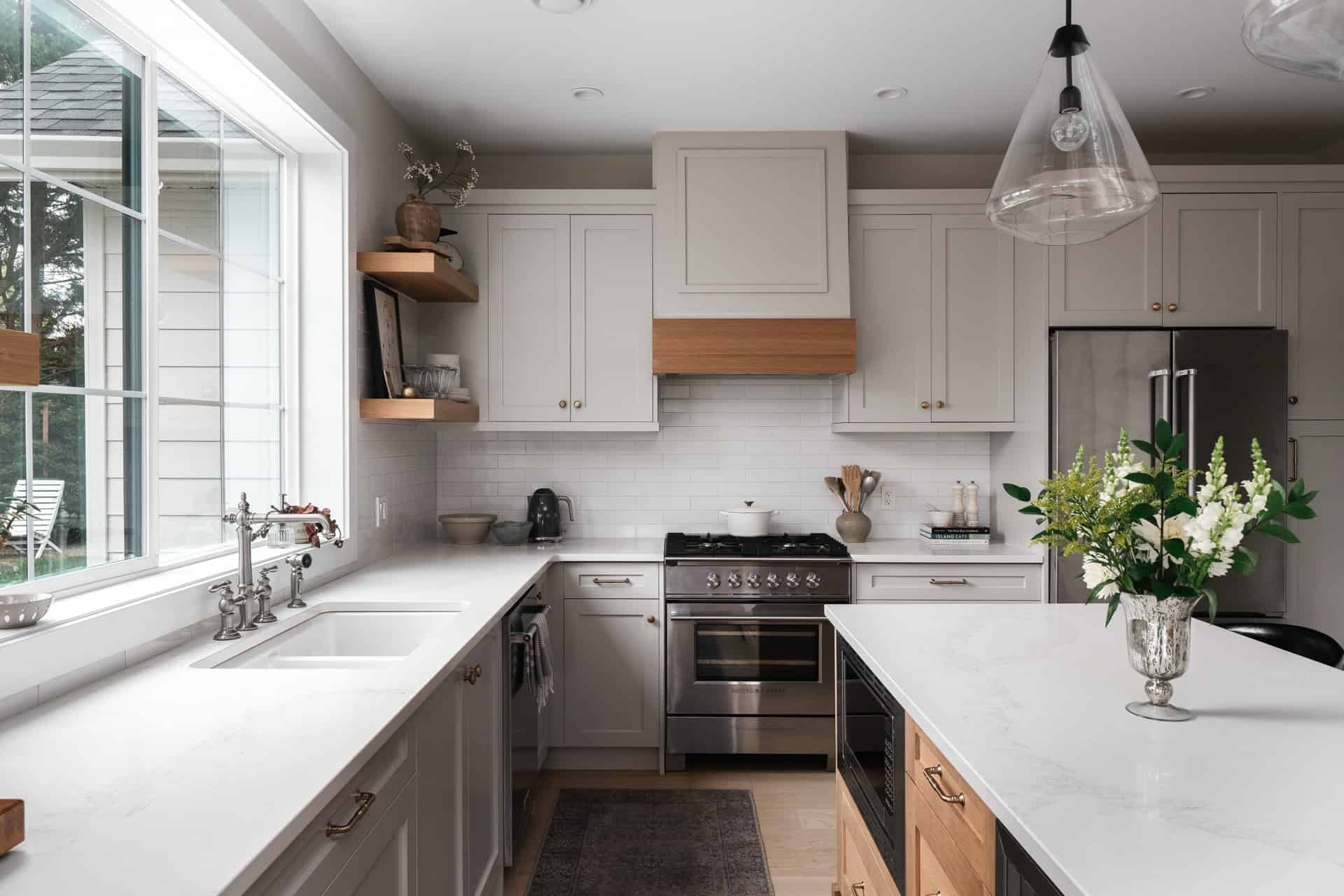 Modern white kitchen with island, stainless steel appliances, and large window.