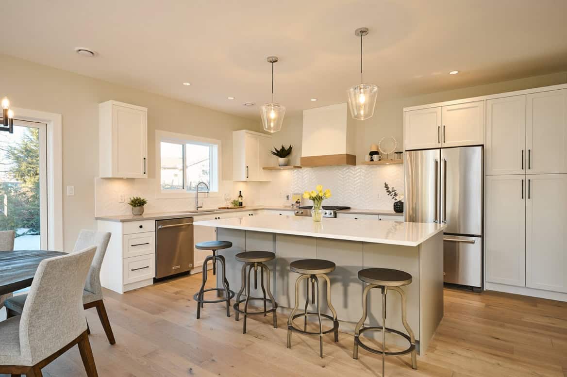 Modern white kitchen with island, pendant lights, and stainless appliances in Meadowview home by White Wolf Homes.