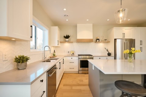 Modern white kitchen with island, stainless steel appliances and light wood floors.