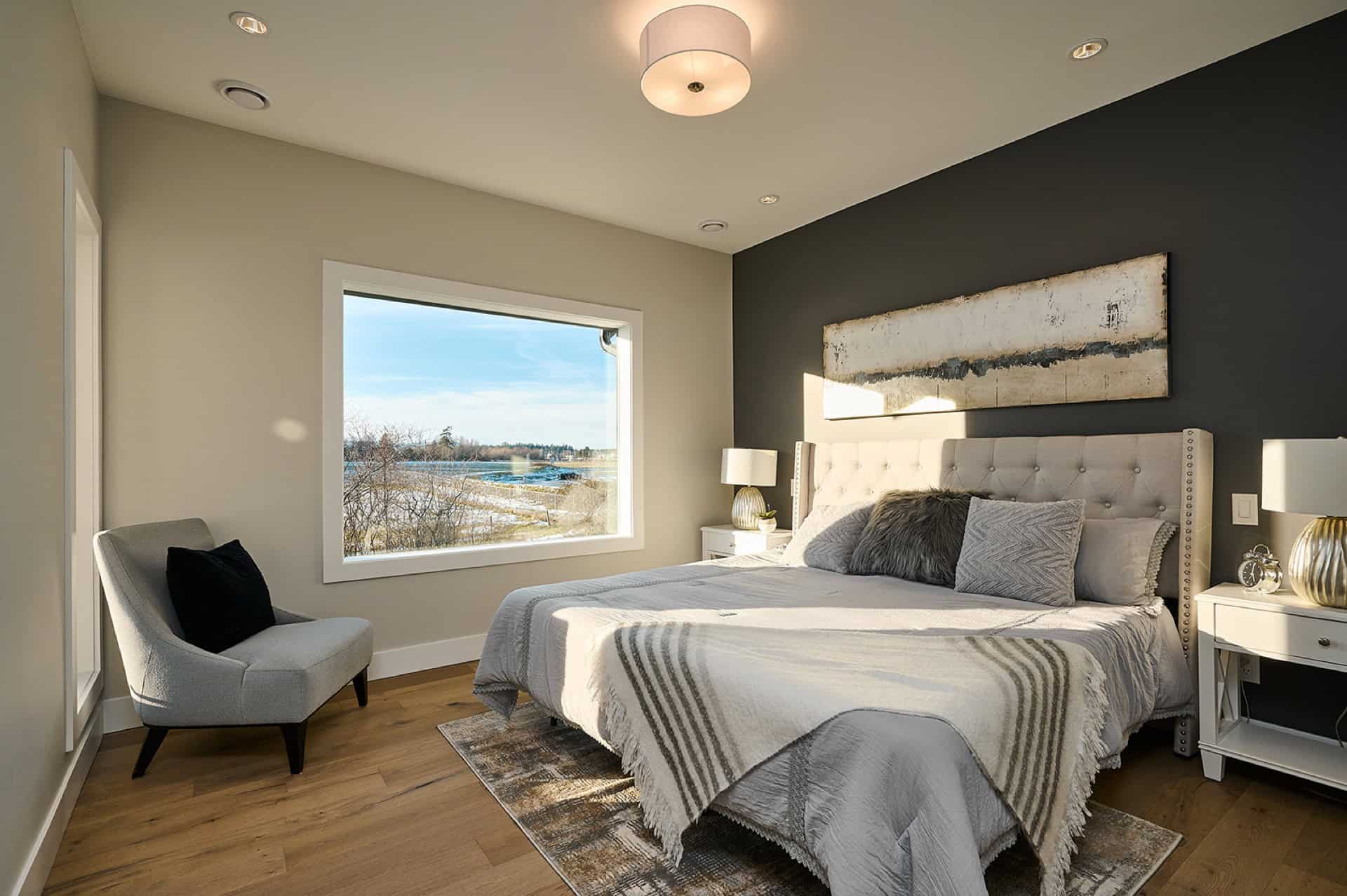 Modern master bedroom with large window, neutral tones, and upholstered headboard.