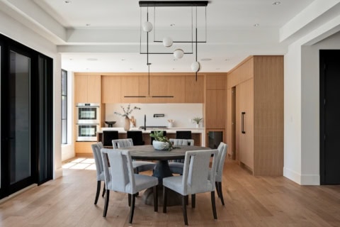 Open-concept dining and kitchen area with wooden cabinetry, round table, and modern pendant lighting.