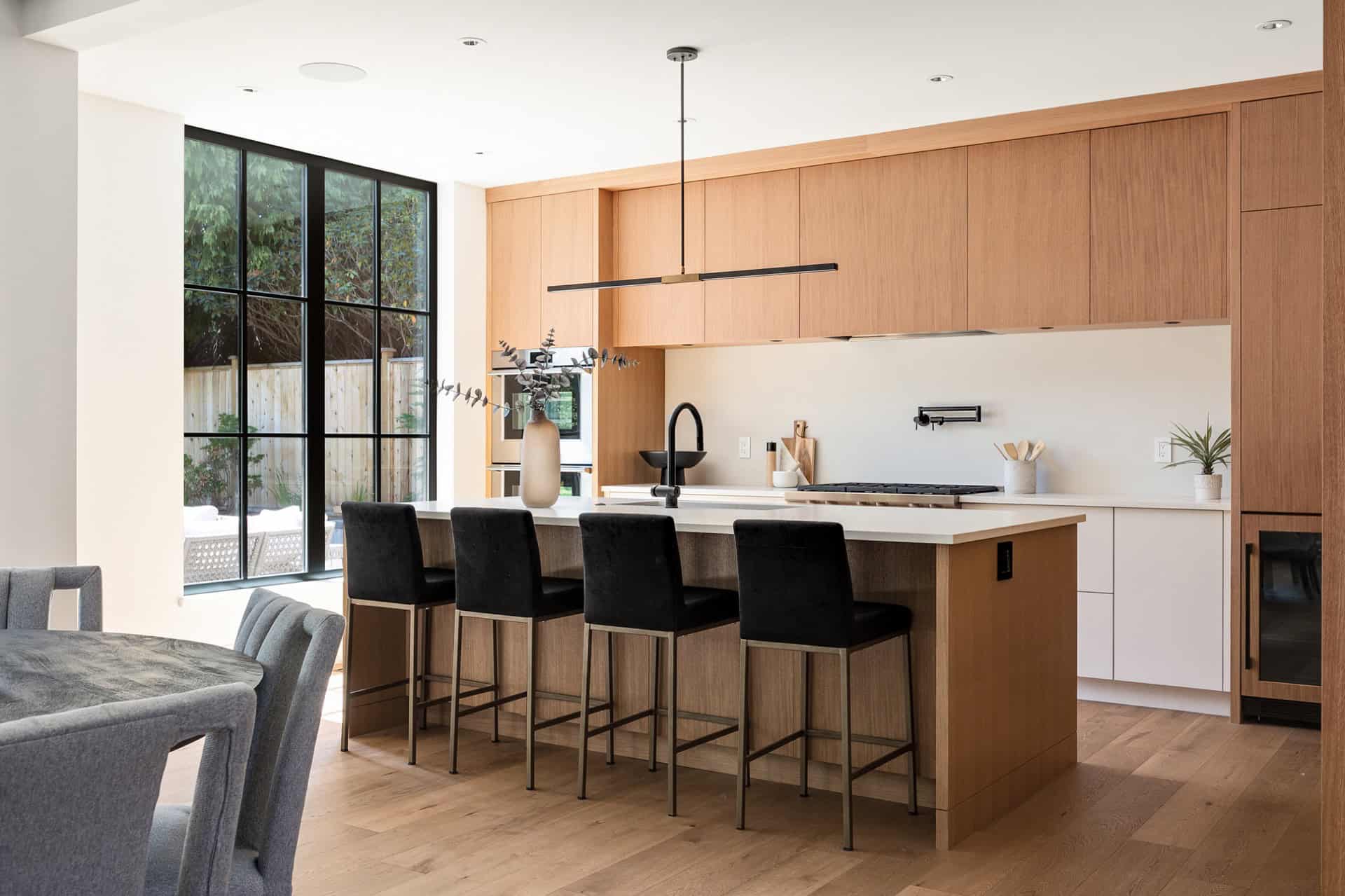 Modern kitchen with island, wooden cabinetry and black bar stools.