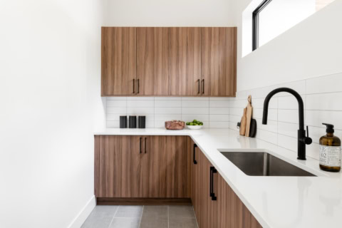 Modern wood-toned kitchen cabinets with white countertops and a black faucet.