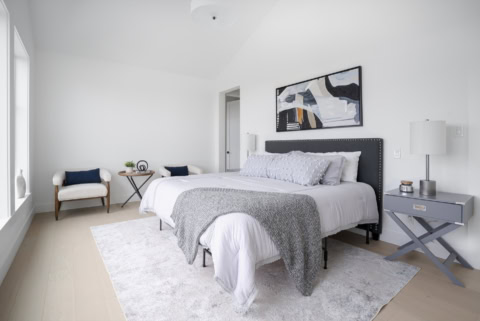 Bright modern bedroom with a gray upholstered bed, matching nightstands, and abstract wall art.
