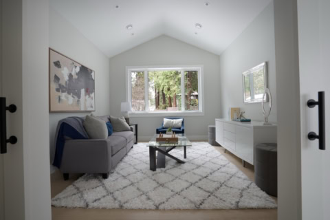 Bright living room with gray sofa, white rug, and glass coffee table in a modern home.