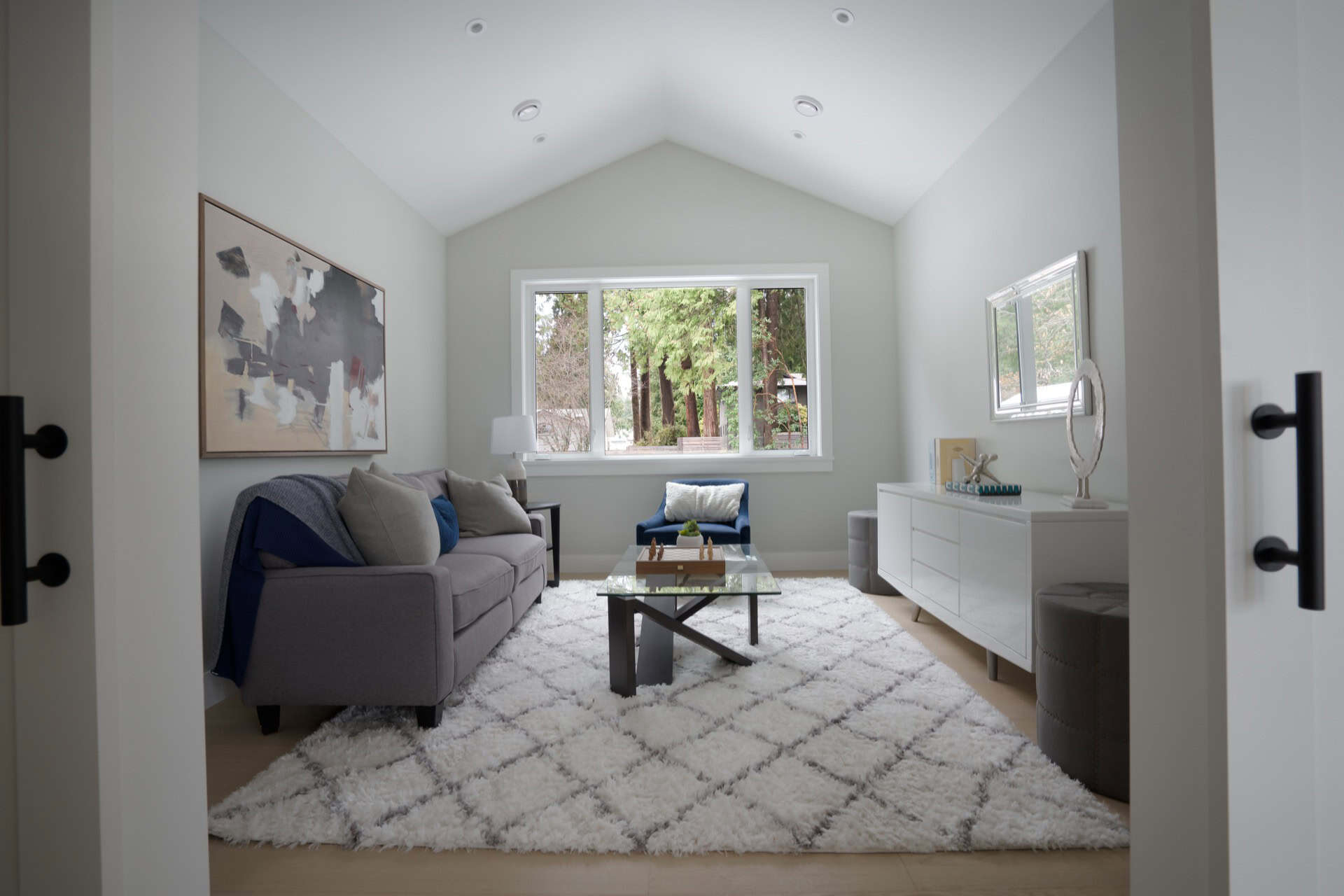 Bright living room with gray sofa, white rug, and glass coffee table in a modern home.