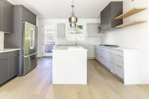 White Wolf Homes kitchen: modern white island, gray lower cabinets, stainless steel appliances.