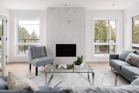 Modern living room with stone fireplace, large windows, and minimalist seating in a bright Victoria BC home.
