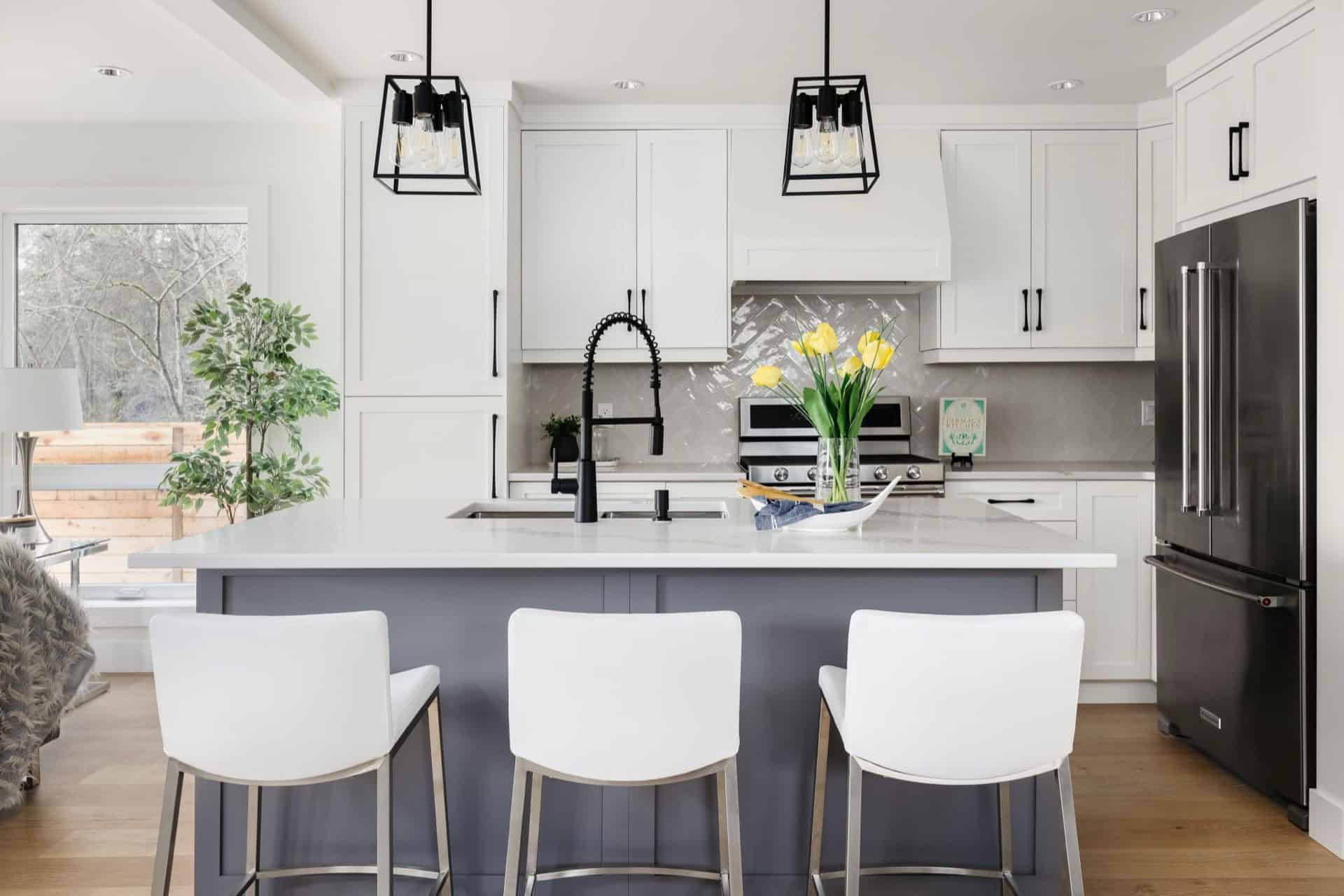 Modern white kitchen featuring island with sink, pendant lights, and yellow flowers.