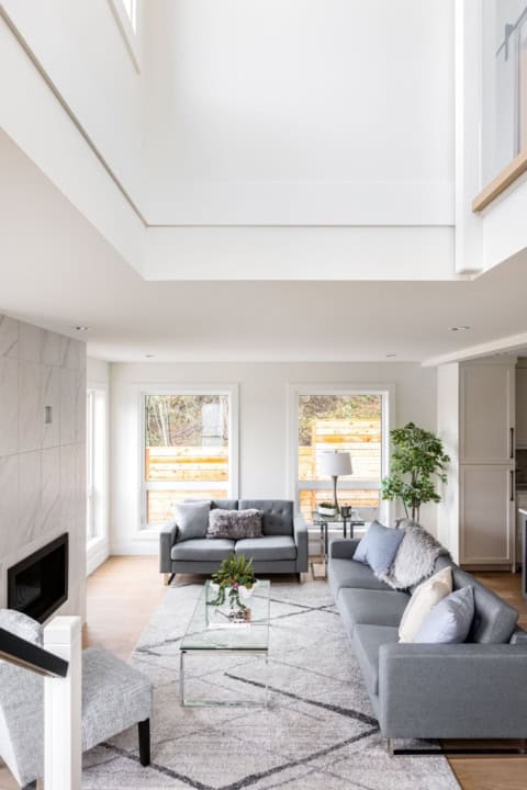 Open concept living room with grey sofas, glass coffee table, and skylight in a bright white modern home.
