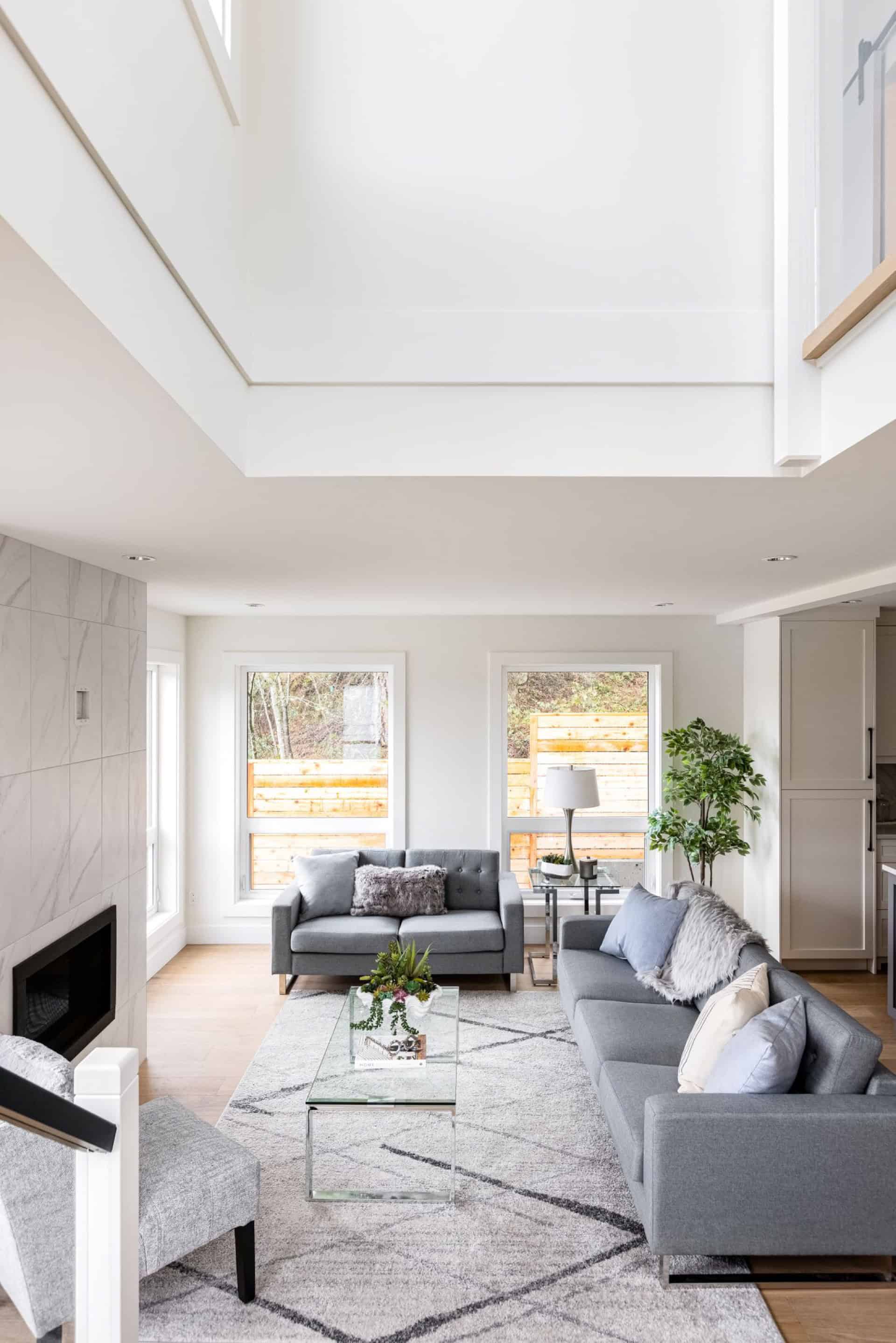 Open concept living room with grey sofas, glass coffee table, and skylight in a bright white modern home.