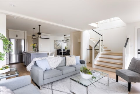 Bright open-concept living room with grey furniture, glass coffee table, and staircase at Arbutus Rise.