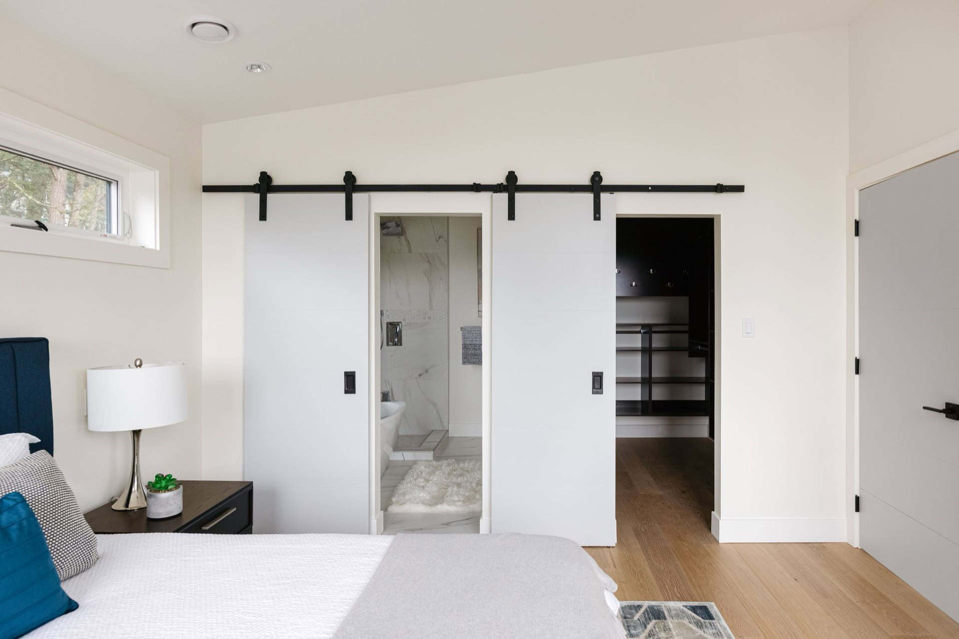 Bright modern bedroom with white walls and sliding barn doors into ensuite and walk-in closet.