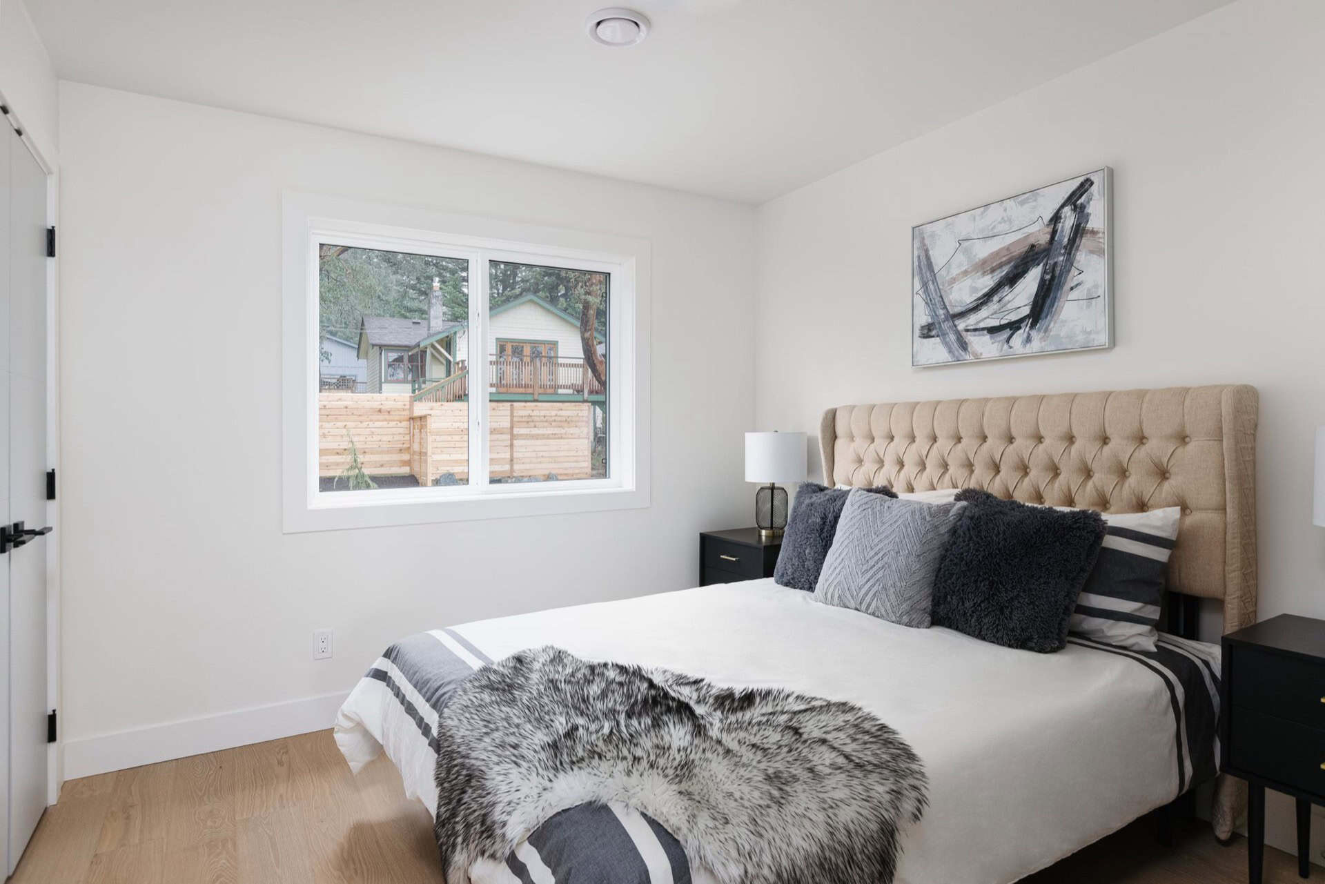Bright bedroom with window view, beige upholstered bed, and modern decor.