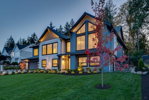 Modern Victoria BC custom home with illuminated interior through large windows and landscaped front yard.
