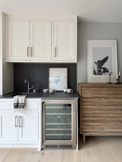 Modern compact kitchen with white cabinets, wine cooler, and wooden sideboard in a light-filled room.