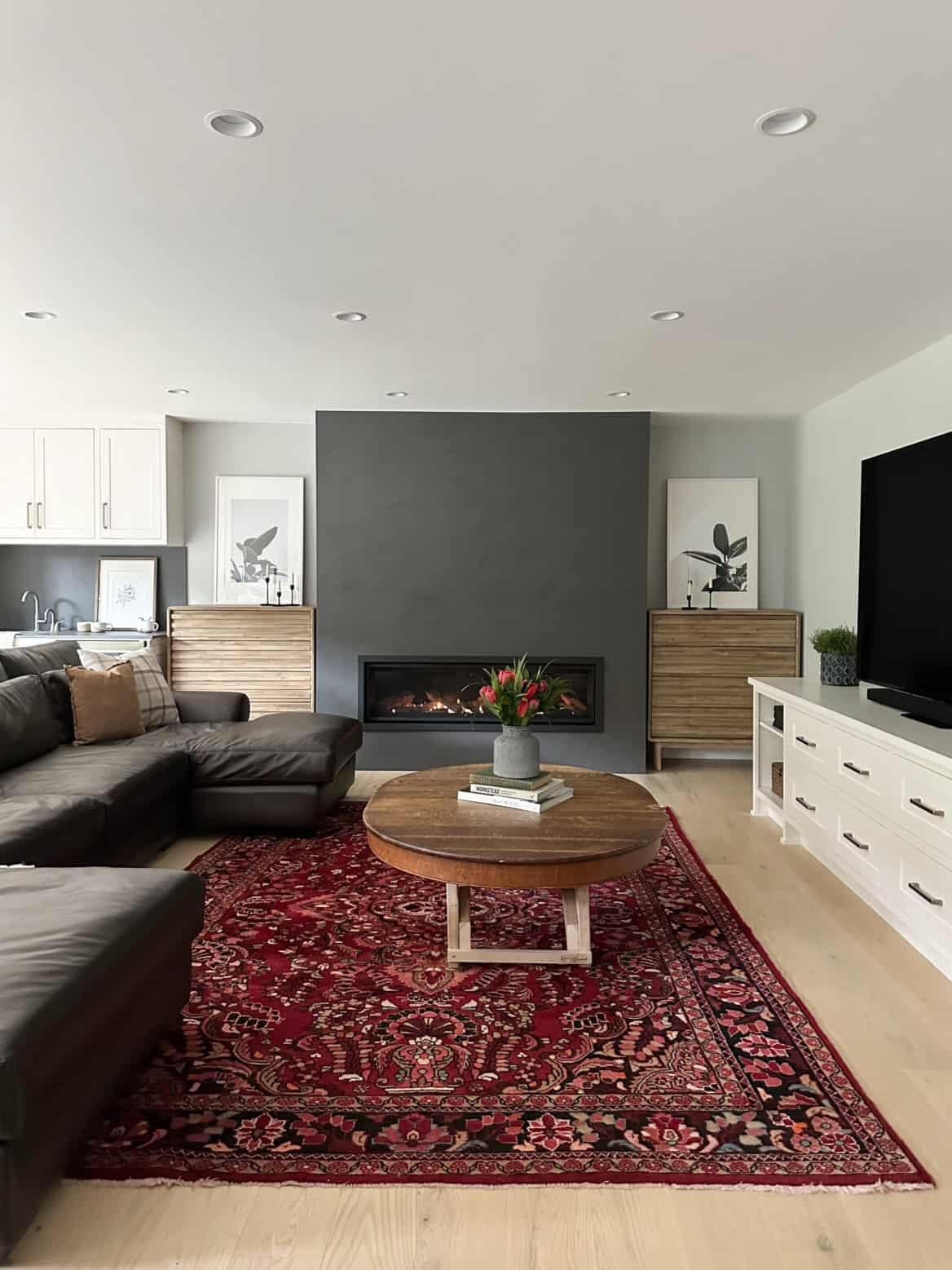 Modern living room with fireplace, dark accent wall, and red patterned rug in a bright open-plan home.