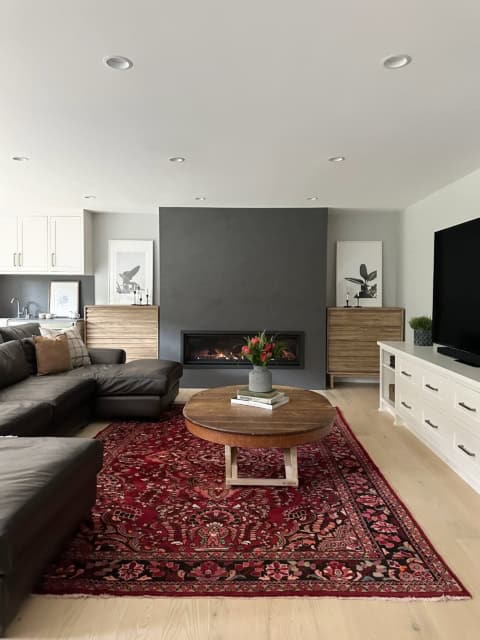 Modern living room with fireplace, dark accent wall, and red patterned rug in a bright open-plan home.