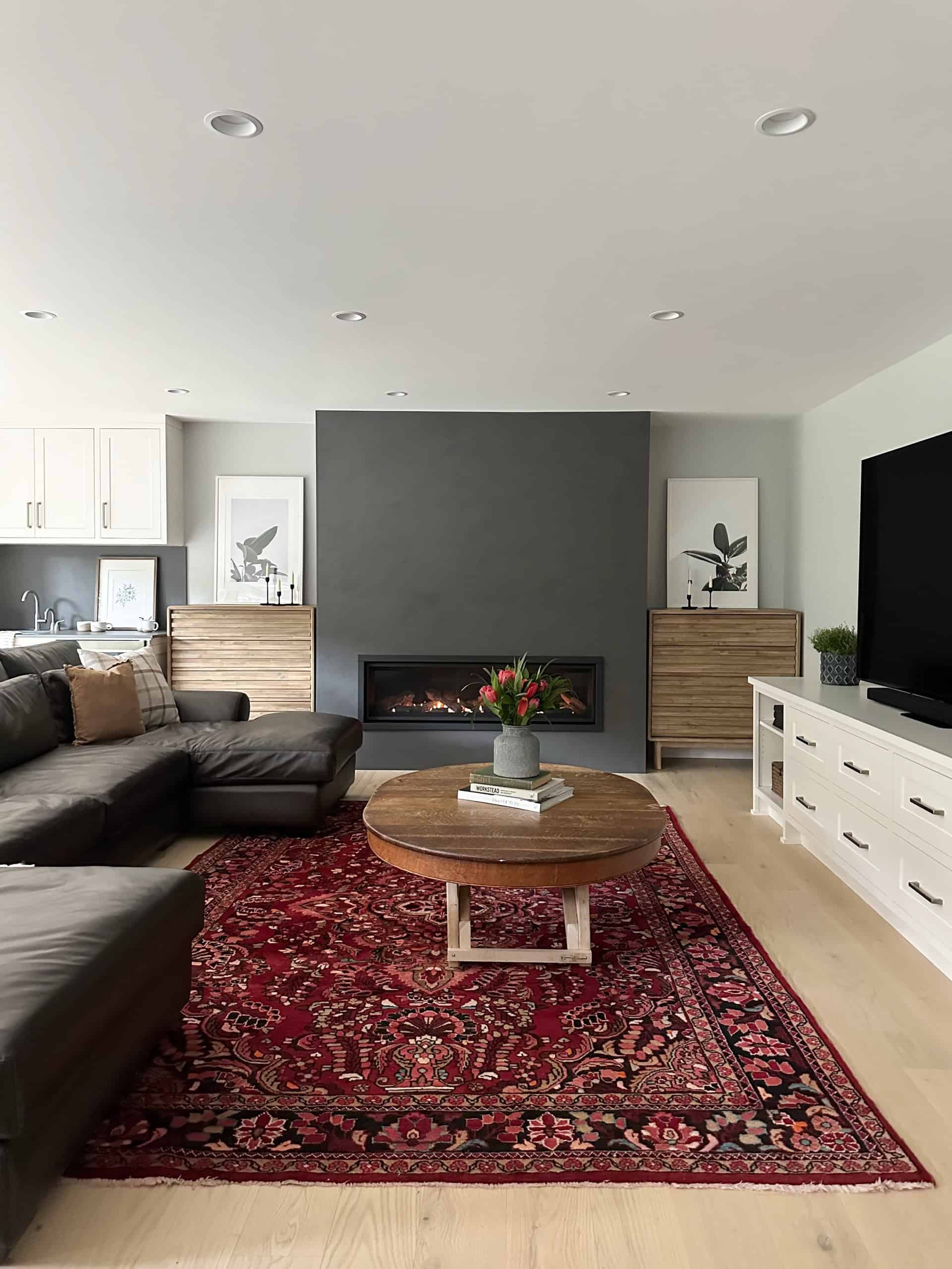 Modern living room with fireplace, dark accent wall, and red patterned rug in a bright open-plan home.