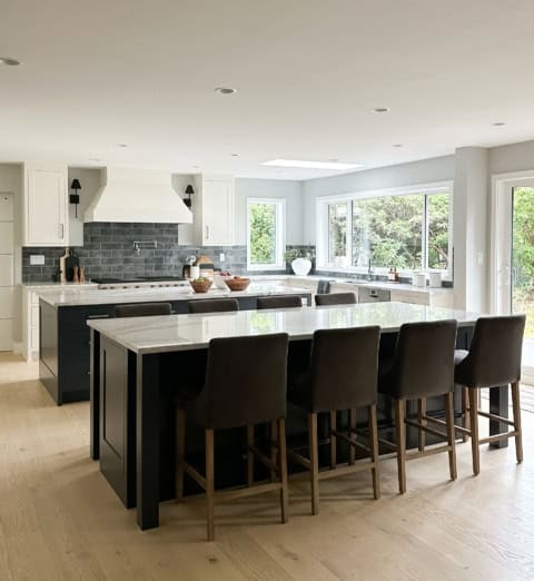Bright modern kitchen with large island and nine stools, white cabinets, and stone backsplash.