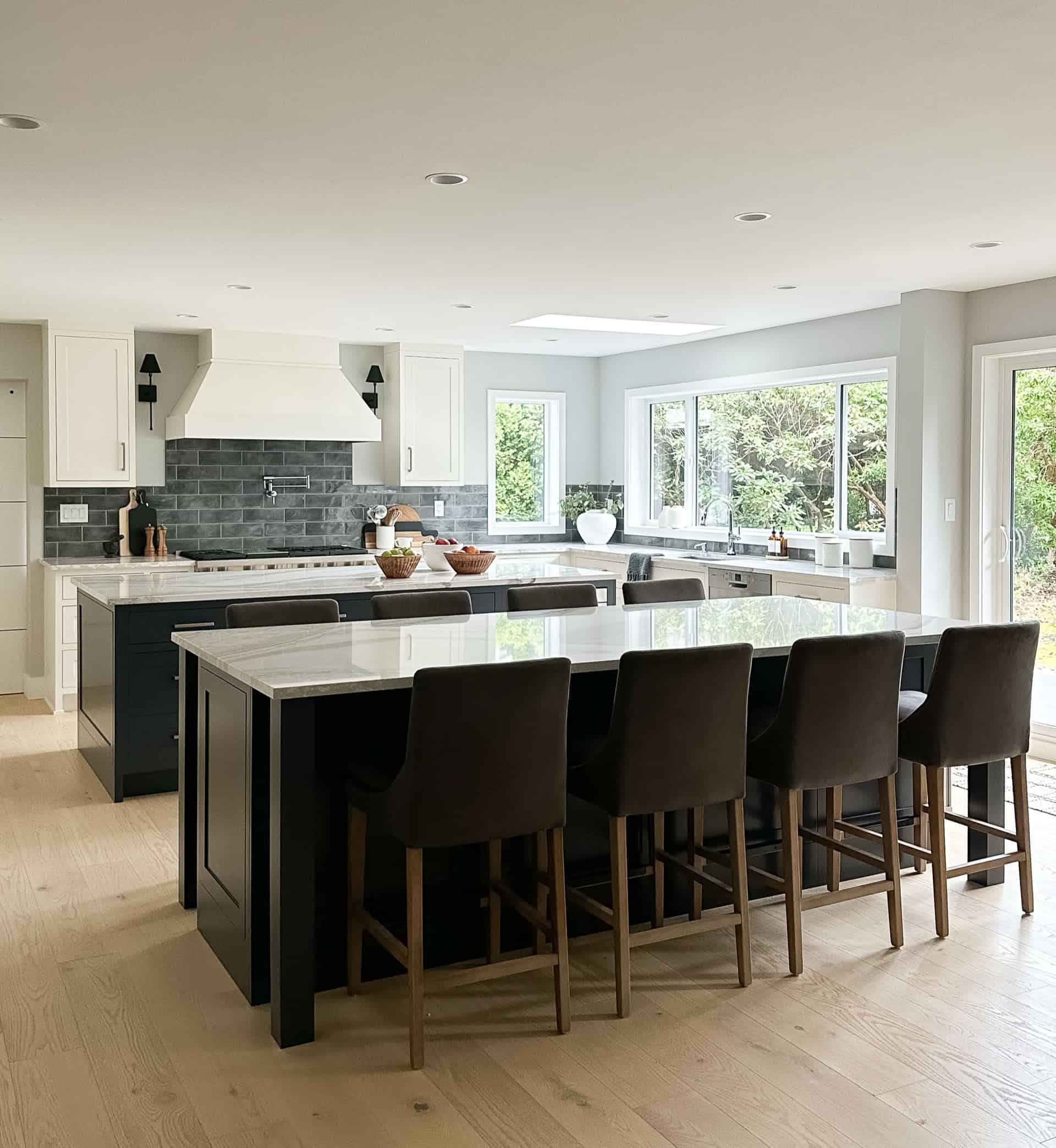Bright modern kitchen with large island and nine stools, white cabinets, and stone backsplash.