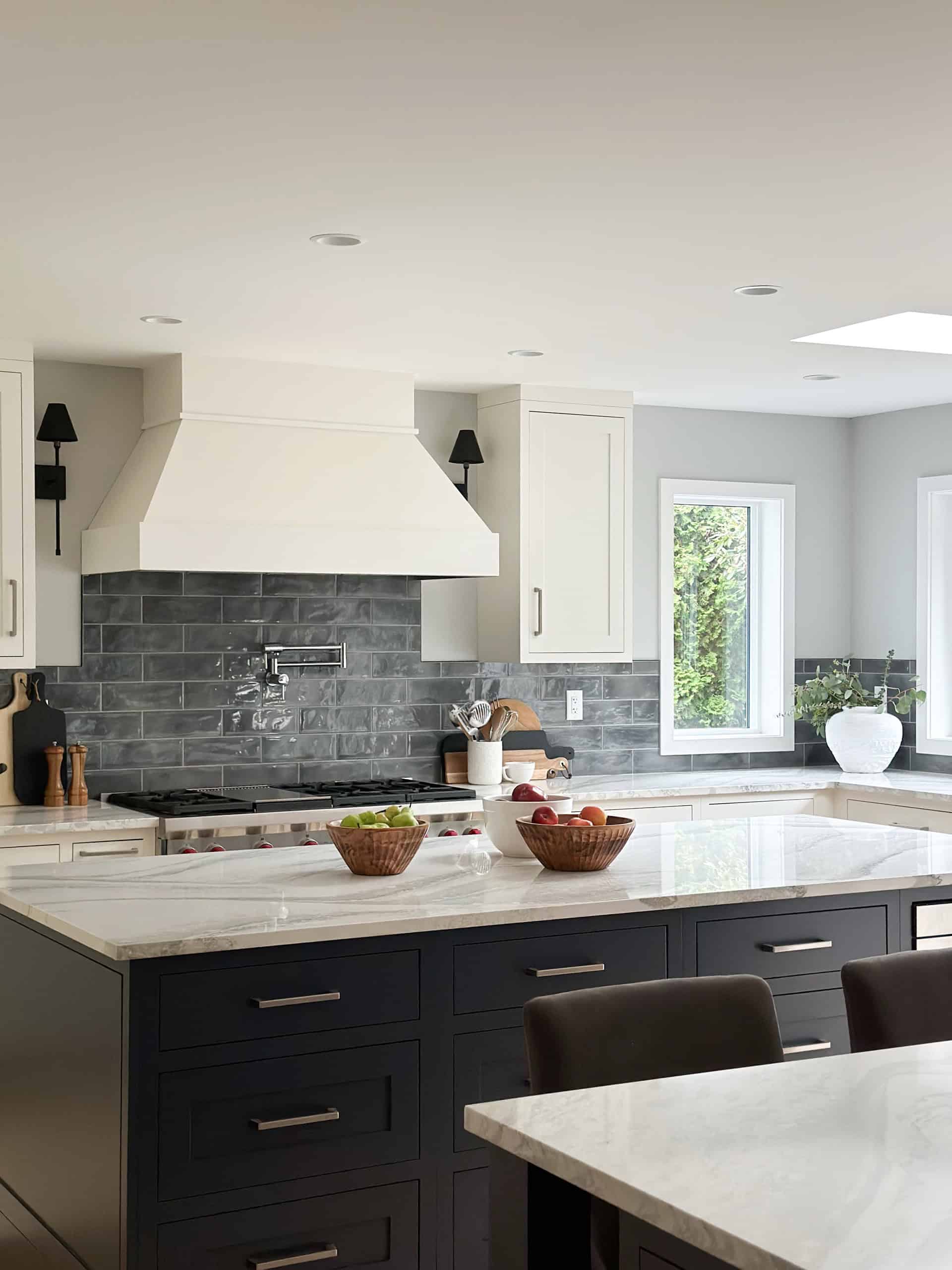 Modern kitchen with white cabinets, dark blue island drawers, and gray subway tile backsplash.