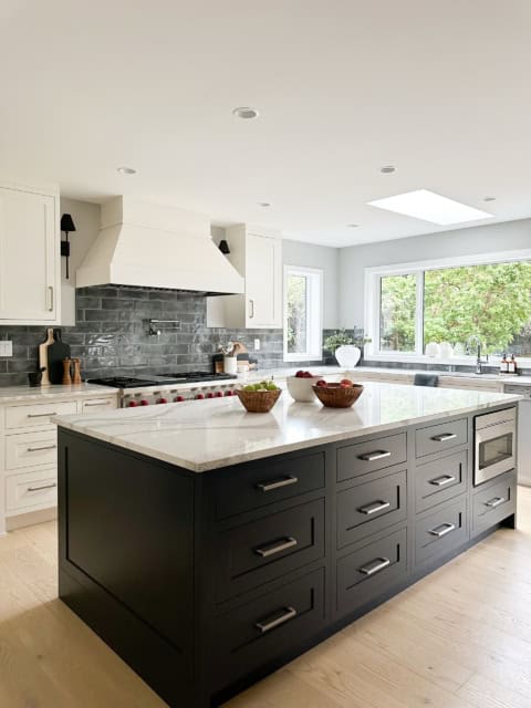 Modern kitchen with an oversized dark island and white cabinetry, bright natural light, and brick accents.