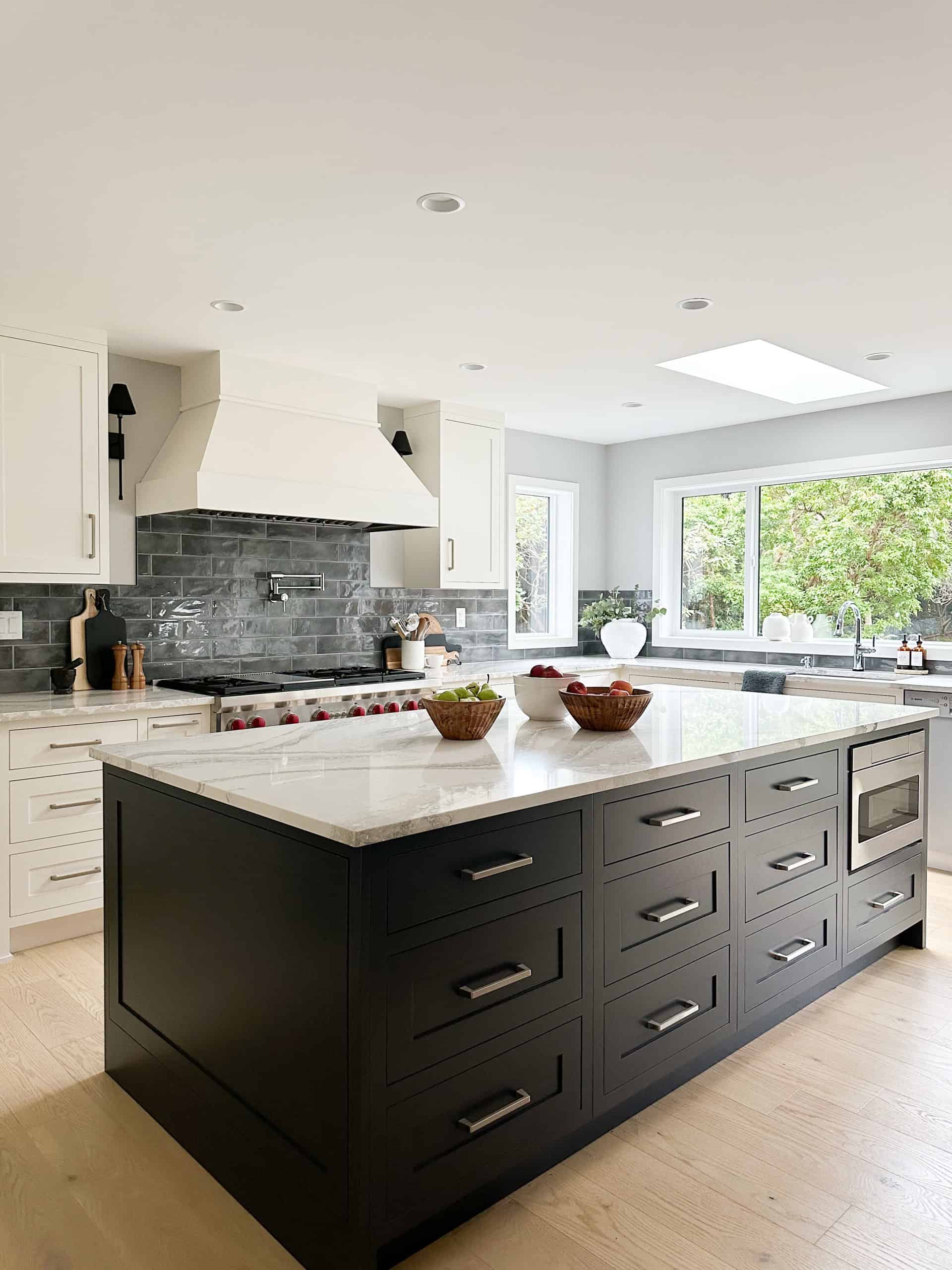Modern kitchen with an oversized dark island and white cabinetry, bright natural light, and brick accents.