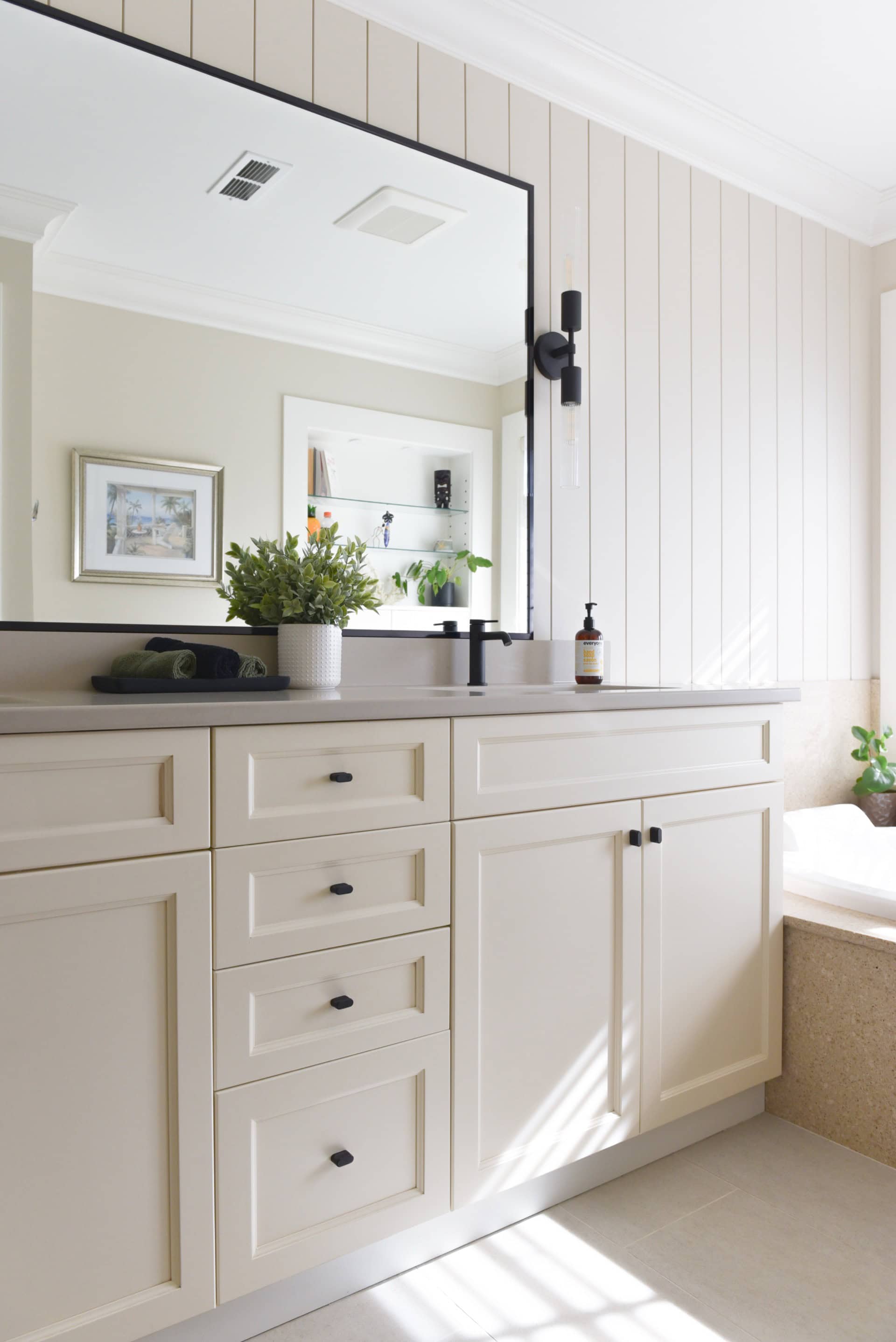 Bright modern bathroom vanity with white cabinetry, large mirror, and potted plant.