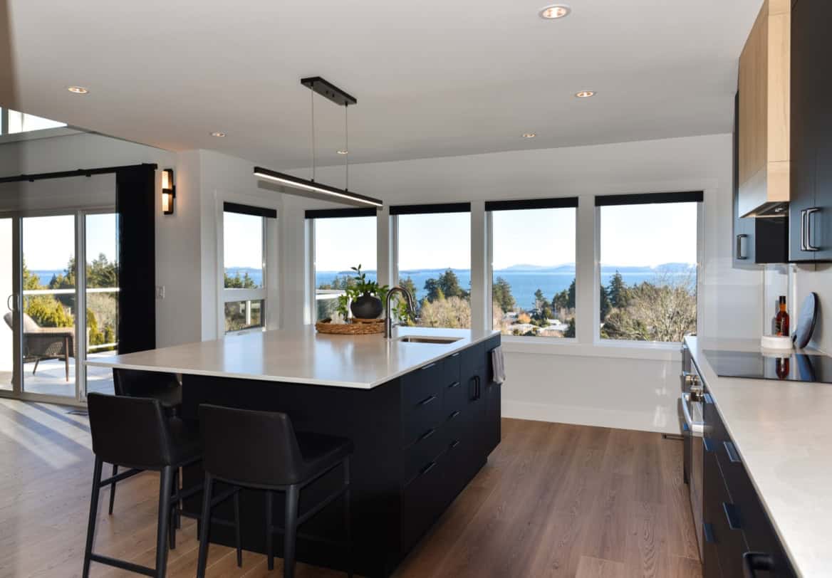 Modern kitchen with large island and expansive windows overlooking ocean in Victoria, BC.