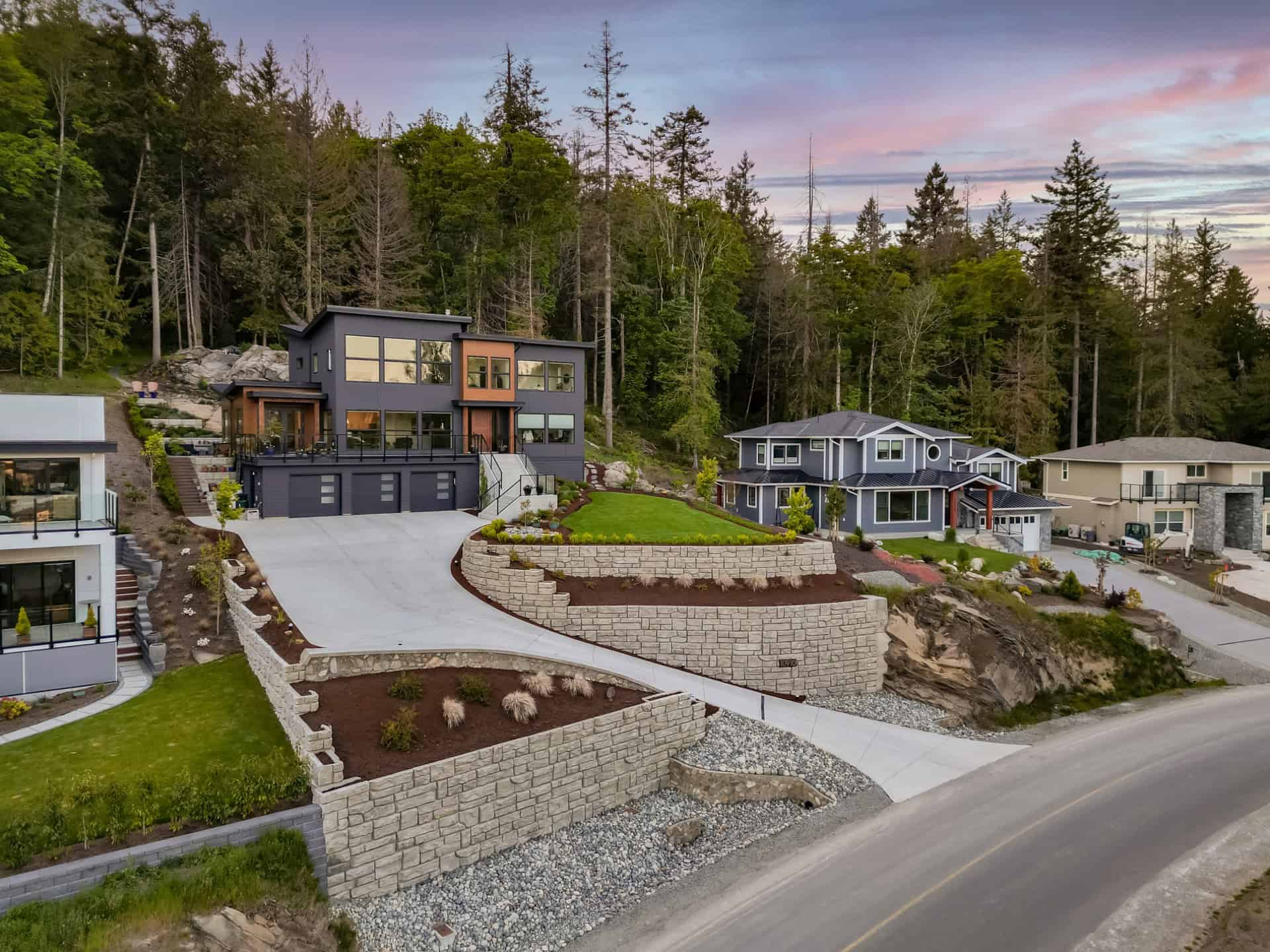 Victoria BC custom home by White Wolf Homes on hillside, modern dark exterior, stone retaining walls.