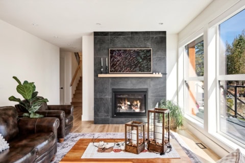 Bright living room featuring a modern fireplace with dark tile surround and large windows.
